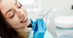 A woman benefits from the services of a Maxillofacial Surgeon while getting her teeth cleaned in a dentist's office.